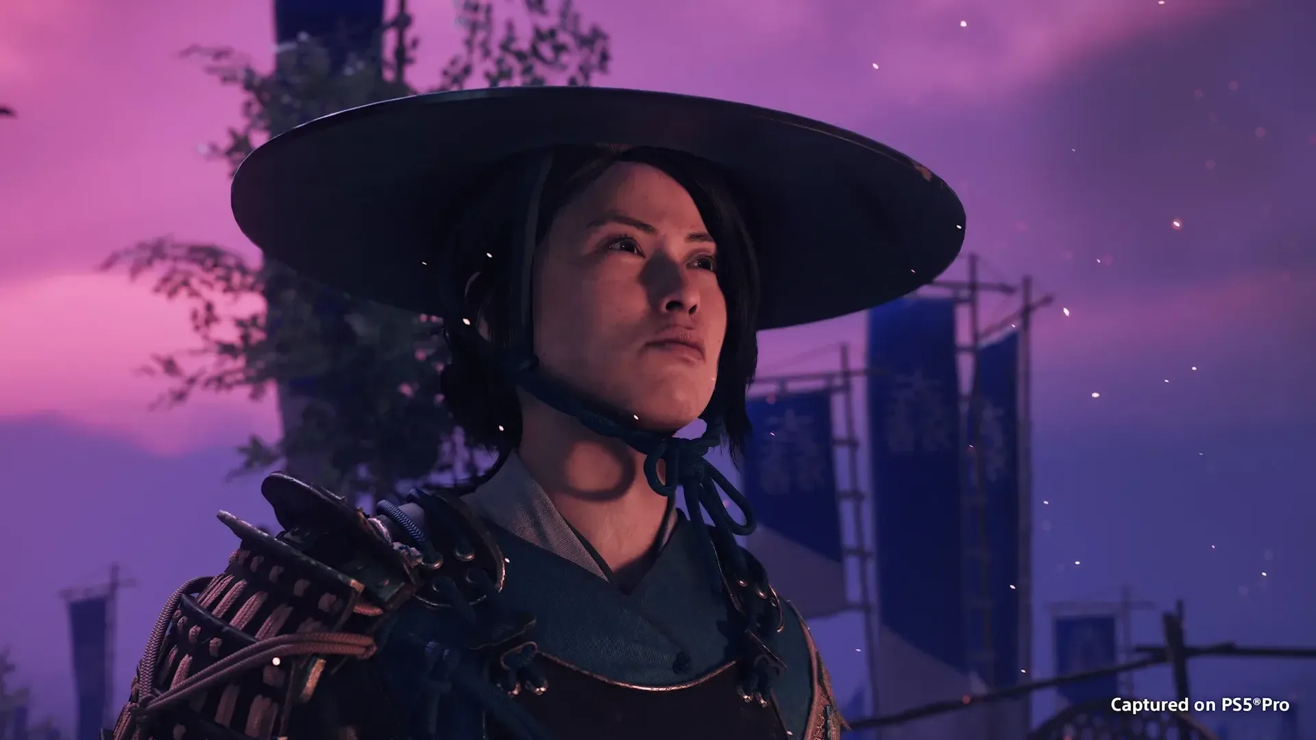 Primer plano de la protagonista de Ghost of Yotei con sombrero tradicional y armadura bajo un cielo crepuscular.